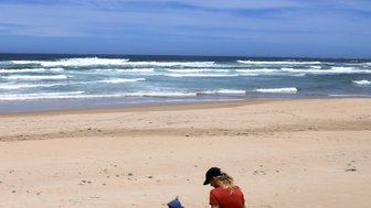 Kind sitzt mit Mutter im Sand und schaut aufs Meer – Garden Route Familienreise
