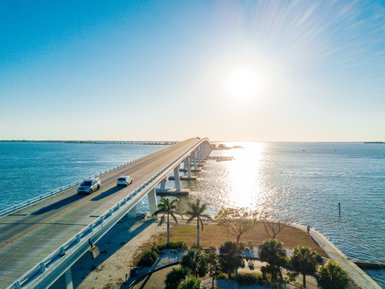 Eine malerische Brücke erstreckt sich über das glitzernde Wasser, während Autos in der warmen Sonne fahren.