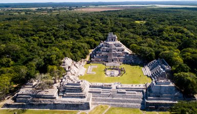 Eine beeindruckende Sicht auf die Ruinen einer alten Maya-Stadt, umgeben von üppigem Grün und einem klaren blauen Himmel.