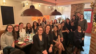 Eine Gruppe von Frauen sitzt in einem gemütlichen Restaurant, umgeben von warmem Licht und festlicher Dekoration.