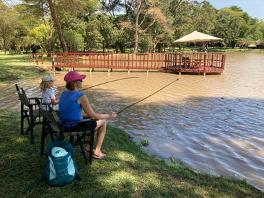 Eine Frau und ein Kind sitzen am Ufer eines ruhigen Gewässers und angeln entspannt in der Natur.
