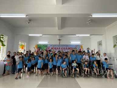Eine fröhliche Gruppe von Kindern und Betreuern posiert in blauen T-Shirts in einem hellen Raum mit bunten Dekorationen.
