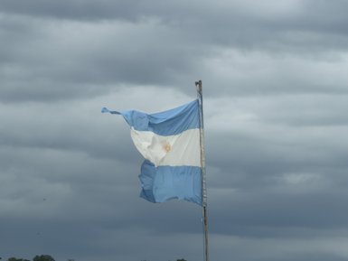 Eine argentinische Flagge weht stark im Wind vor einem dramatischen, wolkigen Himmel.
