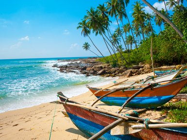 Sandstrand mit Booten neben dem klaren Wasser und Palmen im Hintergrund – Sri Lanka mit Kindern