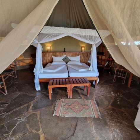 Ein gemütliches Zeltzimmer mit zwei Einzelbetten, umgeben von Moskitonetzen und rustikalen Holzmöbeln.