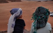 Zwei Kinder sitzen auf einem Felsen und blicken auf die weite Wüstenlandschaft bei Sonnenuntergang.