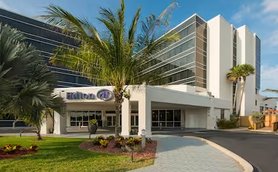 Das Hilton Hotel in Cocoa Beach präsentiert sich mit moderner Architektur und üppiger tropischer Vegetation im Vordergrund.