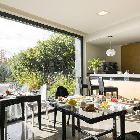Ein eleganter Frühstücksraum mit einem Tisch voller köstlicher Speisen und Blick auf einen grünen Garten durch große Fenster.