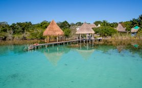 Ein ruhiger Wasserblick auf eine Holzplattform mit einem Strohdach, umgeben von klarem, türkisfarbenem Wasser und üppiger Vegetation.