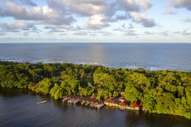 Das atemberaubende Bild zeigt eine friedliche Lodge am Wasser, umgeben von üppigem Grün und dem weiten Ozean im Hintergrund.