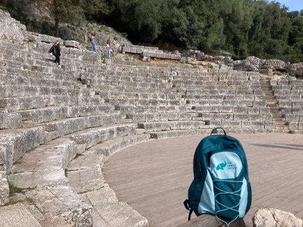 Eine Gruppe von Menschen erkundet die steinernen Stufen eines antiken Theaters, während ein Rucksack im Vordergrund steht.