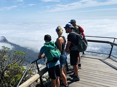 Eine Gruppe von vier Wanderern steht an einem Aussichtspunkt und blickt auf die Wolkenlandschaft unter ihnen.