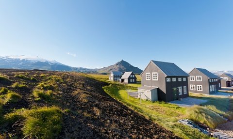 Eine malerische Landschaft mit modernen, schwarzen Ferienhäusern vor einem majestätischen Berg und klarem Himmel.