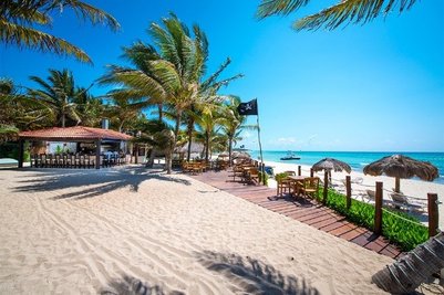 Ein sonniger Strand mit Palmen, einem Restaurant im Hintergrund und einem Boot, das sanft auf dem Wasser schaukelt.