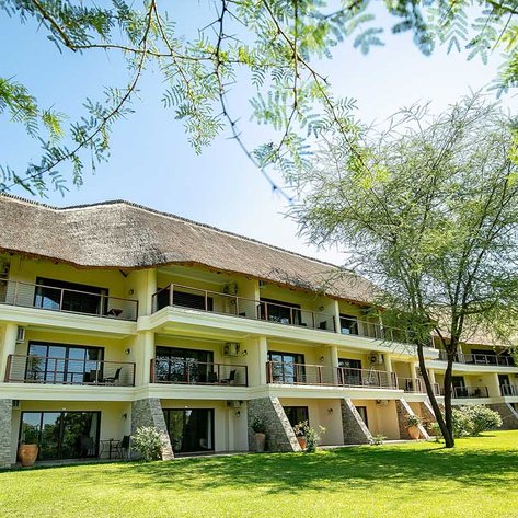 Das Ilala Lodge Hotel in Botswana zeigt eine moderne Architektur mit einem traditionellen Strohdach und einem gepflegten Garten.