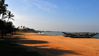 Kleines Boot liegt am orangenen Sandstrand vor tropischer Kulisse – Sri Lanka Familienreise