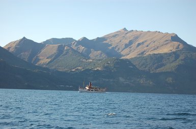 Ein historisches Dampfschiff fährt ruhig über den glitzernden Lake Wakatipu, umgeben von majestätischen Bergen.