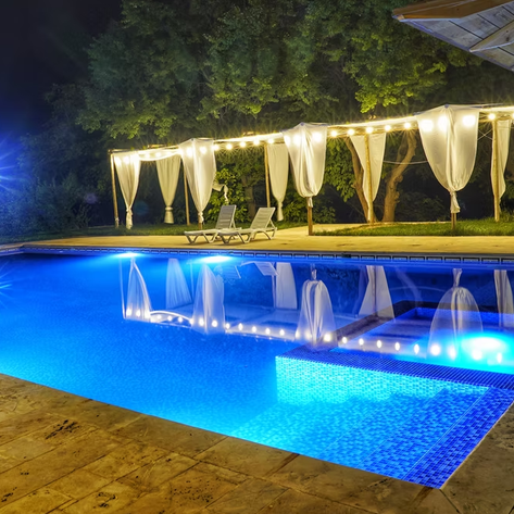 Ein beleuchteter Pool in der Nacht, umgeben von sanften Vorhängen und Liegen, schafft eine entspannende Atmosphäre.