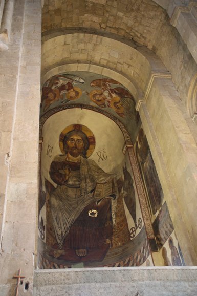 Ein beeindruckendes Wandgemälde zeigt Christus, der ein Buch hält, umgeben von himmlischen Wesen und religiösen Symbolen.