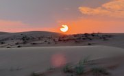 Ein atemberaubender Sonnenuntergang über den sanften Dünen, die in warmen Farben leuchten und die Stille der Wüste widerspiegeln.