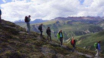 Eine Gruppe von Wanderern erkundet die hügelige Landschaft des Yukon mit beeindruckenden Bergen im Hintergrund.