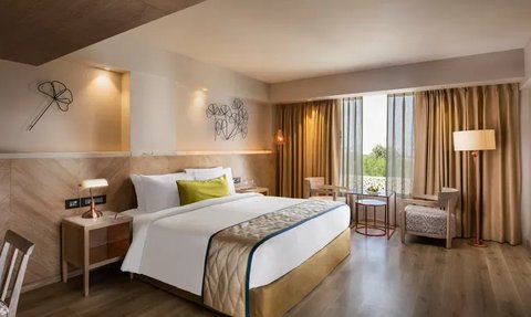 Ein modernes Hotelzimmer mit einem großen Bett, eleganten Möbeln und viel natürlichem Licht durch die Fenster.