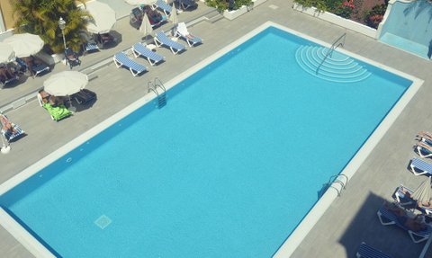 Ein klarer Pool mit sanften Wellen und einer Treppe, umgeben von Liegen und Sonnenschirmen, ideal für Entspannung.