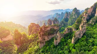 Eine atemberaubende Aussicht auf grüne Berge, die in der Morgensonne leuchten, mit schroffen Felsen und üppiger Vegetation.