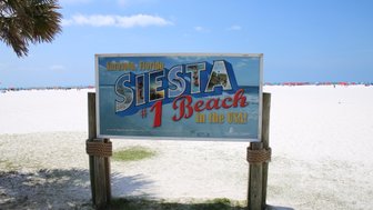 Ein großes Schild verkündet, dass Siesta Beach in Sarasota, Florida, der beste Strand in den USA ist, umgeben von weißem Sand.