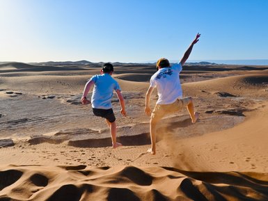 Kinder springen und haben Spaß auf den weiten Sanddünen der Sahara – Marokko Familienreise