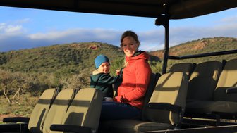 Mutter und Kind genießen gemeinsam die Safari im offenen Jeep und lächeln in die Kamera – Garden Route Reise mit Kindern