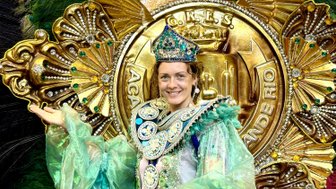 Eine festlich gekleidete Person strahlt Freude aus, gekleidet in einem glitzernden grünen Kostüm mit prachtvollen Verzierungen.