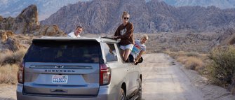 Eine Familie genießt einen Roadtrip in der Wüste, während sie fröhlich aus einem SUV herausblickt.