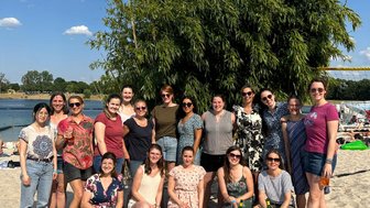 Eine Gruppe von Frauen posiert fröhlich am Strand, umgeben von grünem Bambus und strahlend blauem Himmel.