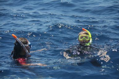 Ein Junge und ein Mädchen schwimmen fröhlich im klaren blauen Wasser, beide tragen Schnorchel und Taucherbrillen.