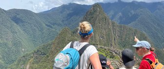 Eine Gruppe von Menschen steht auf einem Aussichtspunkt und bewundert die Ruinen von Machu Picchu inmitten der Berge.