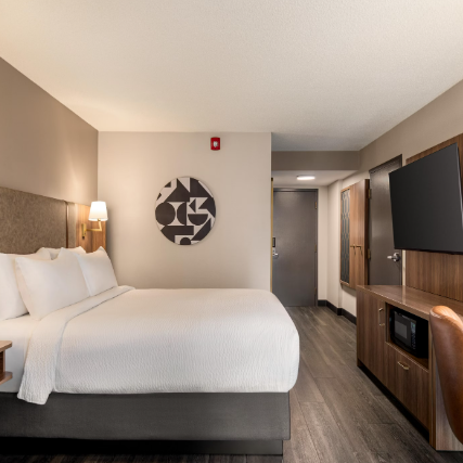 Ein modernes Hotelzimmer mit einem großen Bett, einem Schreibtisch und einem Fernseher an der Wand.