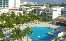 Ein weitläufiger Pool umgeben von Palmen und modernen weißen Gebäuden, ideal für einen entspannten Urlaub in Mexiko.