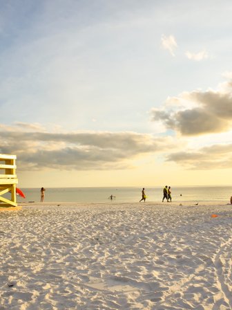 Ein leuchtend gelbes Rettungshaus steht am Strand, während Menschen im warmen Sonnenlicht spazieren gehen.