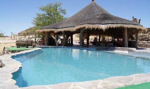 Ein einladender Pool in der Wüste, umgeben von einem strohgedeckten Pavillon und karger Landschaft.