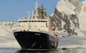 Das Forschungsschiff Ortelius liegt vor schneebedeckten Bergen in der Antarktis, während ein kleines Boot ablegt.