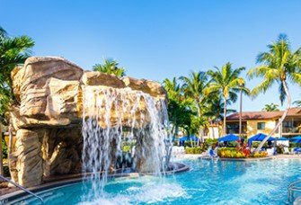 Ein malerischer Pool mit einem Wasserfall, umgeben von Palmen und Sonnenliegen, ideal für Entspannung und Erholung.