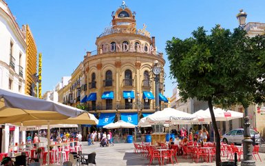 Ein belebter Platz in Jerez mit einem historischen Gebäude, blauen Markisen und vielen Menschen, die die Atmosphäre genießen.