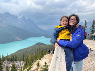 Eine Frau umarmt ein lächelndes Kind an einem Aussichtspunkt mit Blick auf den türkisfarbenen Peyto Lake und die umliegenden Berge.