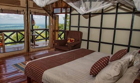 Ein gemütliches Zimmer mit einem großen Bett, umgeben von Moskitonetzen und einem Blick auf die Landschaft durch große Fenster.