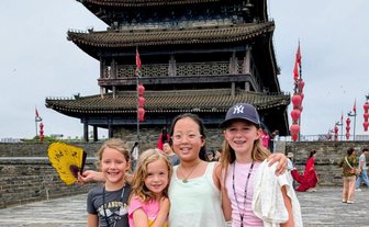 Vier Mädchen stehen fröhlich vor einem historischen Torturm in Xi'an und lächeln in die Kamera, während bunte Laternen im Hintergrund schweben.
