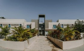 Ein modernes Gebäude mit großen Fenstern und einem klaren Eingang, umgeben von üppigem Grün und einem gepflasterten Weg.