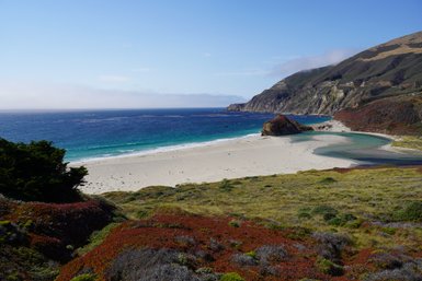 Ein atemberaubender Blick auf einen ruhigen Strand, umgeben von sanften Hügeln und klarem, blauem Wasser.