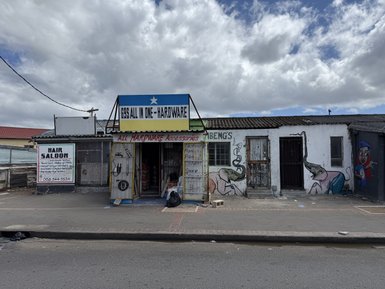 Ein farbenfrohes Geschäft mit einem großen Schild, das 'ALL IN ONE - HARDWARE' anzeigt, umgeben von lebhaften Wandmalereien.