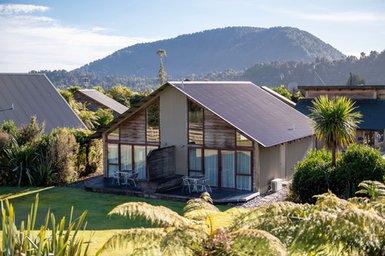 Ein modernes Ferienhaus mit großen Fenstern, umgeben von üppigem Grün und Blick auf sanfte Hügel im Hintergrund.